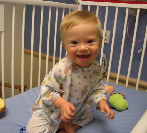 A young boy with down syndrome sitting in a crib.